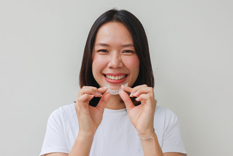 close up young woman smiling with hand holding dental aligner retainer