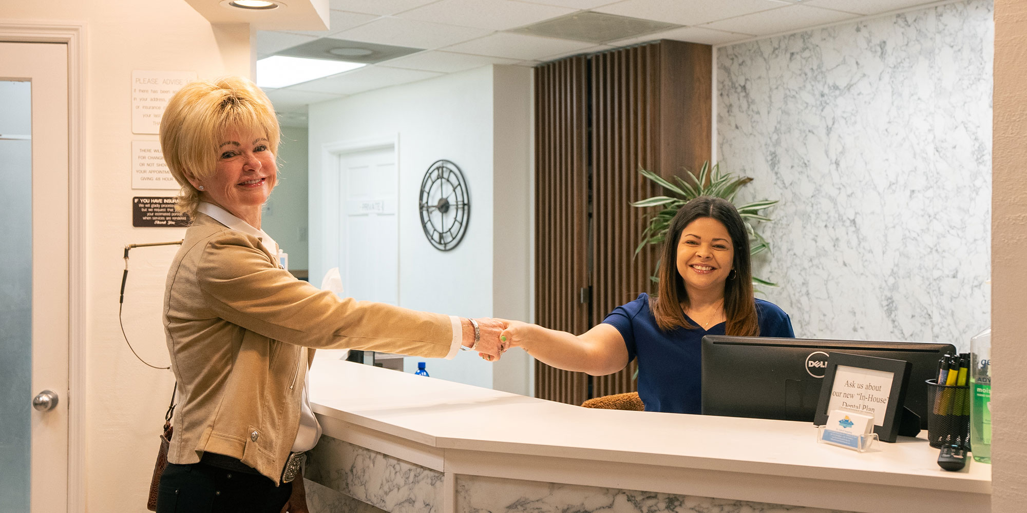 patient and staff member shaking hands at the front desk of the dental center